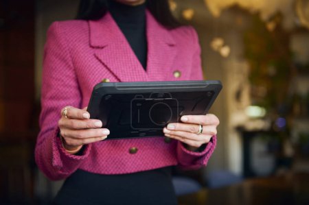 Téléchargez les photos : Details on digital tablet in the hands of a restaurateur, businesswoman in bright purple casual wear, executive director or successful manager, CEO against blurred background of a restaurant interior - en image libre de droit