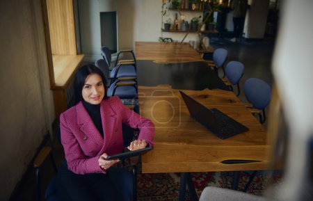 Photo for Confident, attractive, successful, goal-oriented middle-aged Caucasian woman, chief executive, business woman sitting with a tablet at the table and waiting for a meeting with partners and investors - Royalty Free Image