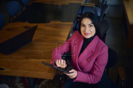 Photo for Attractive purposeful middle aged businesswoman, CEO, holding digital tablet, smiling cutely looking at camera, looking forward to meeting with business partners and investors at the negotiation table - Royalty Free Image