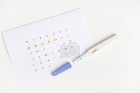 Photo for Flat lay. Positive pregnancy inkjet test and a calendar with the days of the last menstruation marked on white background. Womens health. Ovulation date calculation. Planning pregnancy and maternity - Royalty Free Image