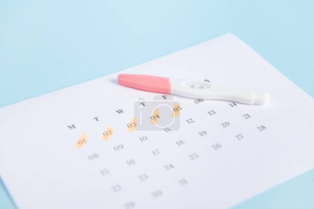 Photo for Selective focus. Pregnancy inkjet test and a calendar with dates of the last menstruation marked on blue color background. Womens health. Ovulation date calculation. Planning pregnancy and maternity - Royalty Free Image