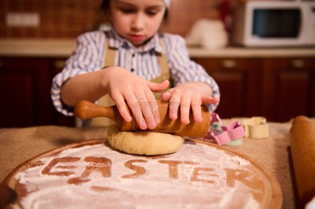 Photo for Details on childs hands using rolling pin, roll out the dough while cooking Easter gingerbread pastries in home kitchen. Lovely little girl dreams to become a chef confectioner, helps mom in cuisine - Royalty Free Image