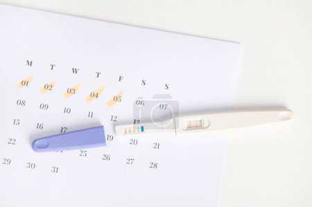 Photo for Top view inkjet pregnancy test with two bars on white calendar with the menstruation last days marked. The concept of calculating ovulation and fertile dates for sure implantation, Planning maternity - Royalty Free Image