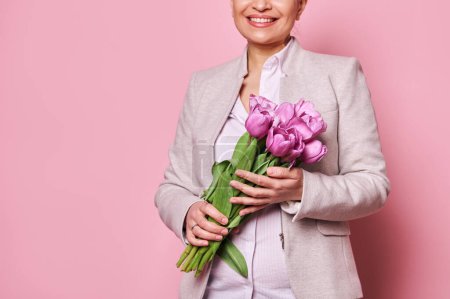 Téléchargez les photos : Détails sur un mignon bouquet de tulipes violettes pour l'occasion festive, entre les mains d'une belle femme souriante, fond rose isolé, Happy Teachers, Mères ou International Womens. Concept de printemps - en image libre de droit