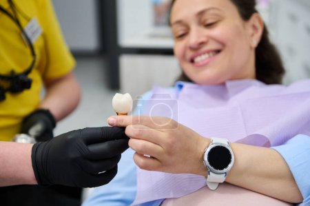 Photo for Selective focus on veneer dental implant sample, in hands of a dentist doctor orthodontist showing dentures - prosthesis and explaining treatment to patient, during dental check up in dentistry clinic - Royalty Free Image