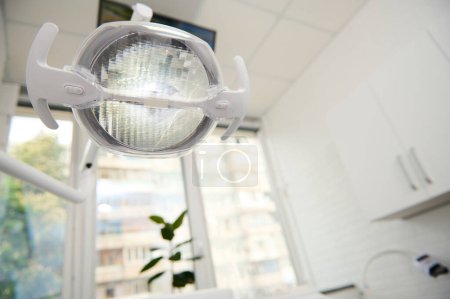 Téléchargez les photos : Matériel dentaire. Une lampe dentaire avec lumière LED directionnelle à l'intérieur blanc clair d'une clinique dentaire moderne. Lampe de fonctionnement. Lampe chirurgicale. Soins de santé et médecine. Copier l'espace publicitaire - en image libre de droit