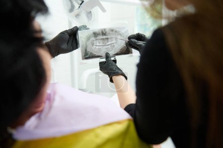Téléchargez les photos : Gros plan image radiographique panoramique dans les mains d'un dentiste médecin montrant à son patient orthopantomogramme des dents humaines, expliquant le traitement qui doit effectuer dans la clinique de dentisterie. Concentration sélective - en image libre de droit