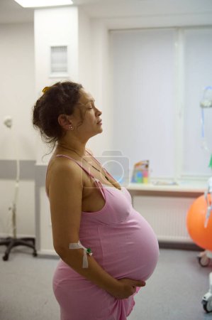 Foto de Mujer embarazada, madre biológica en la sala del hospital, lista para dar a luz a un bebé, sosteniendo el vientre y practicando ejercicios de respiración para inducir un parto fácil. El parto. Concepto de obstetricia y ginecología - Imagen libre de derechos