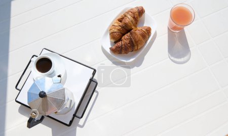 Blick von oben auf den weißen Tisch mit frisch gebackenen französischen Croissants, einem Glas Saft, einer Tasse Espresso, gebrüht im italienischen Perkolator oder Mokka-Brauer. Kopieren Sie Werbeflächen. Guten Morgen Konzept