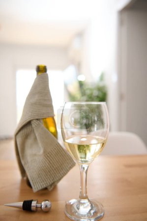 Téléchargez les photos : Nature morte avec un verre à vin et une bouteille de vin mousseux blanc sur une table en bois dans le salon de la maison. Consommation d'aliments et de boissons. Copier l'espace publicitaire - en image libre de droit