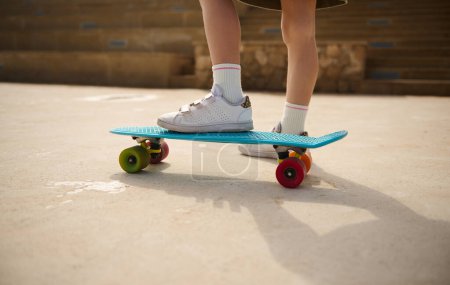 Téléchargez les photos : Jambes de skateboard. Gros plan jambes d'enfant sur une planche à roulettes, planche à roulettes sur une aire de jeux à l'extérieur. Les gens. Mode de vie. Loisirs. Concept de divertissement pour enfants. Le sport extrême. Enfance - en image libre de droit