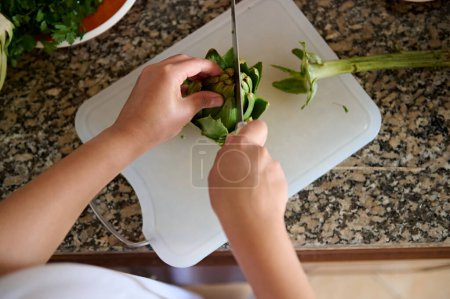 Foto de Vista superior de las manos de una mujer chef de corte y cocción de alcachofa orgánica fresca, de pie junto al mostrador de cocina de mármol. Concepto de dieta saludable. Comida - Imagen libre de derechos