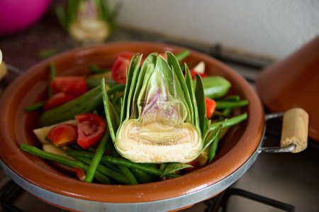 Foto de Enfoque selectivo en la mitad de la alcachofa verde orgánica madura y verduras en el plato de arcilla mientras se cocina el tagine tradicional marroquí. Fondo alimentario - Imagen libre de derechos
