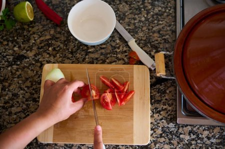 Foto de Vista de cerca desde arriba de un cocinero, usando un cuchillo de cocina cortando tomates cortados en rodajas en una tabla de madera. Fondo alimentario - Imagen libre de derechos