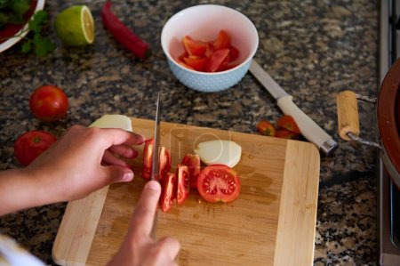 Foto de Vista de cerca desde arriba de un ama de casa picando tomates en una tabla de cortar, cocinar ensalada vegana cruda saludable. Ingredientes tumbados en un mostrador de cocina de mármol - Imagen libre de derechos