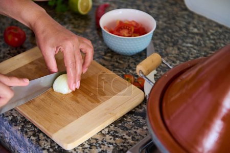 Foto de Vista recortada de las manos de un chef cortando cebolla en dos mitades sobre una tabla de madera, usando un cuchillo de cocina. Ama de casa prepara la cena en la cocina casera. Cocina. Culinario. Vida doméstica - Imagen libre de derechos