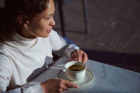 Afro-Américaine belle jeune femme relaxante autour d'une tasse de boisson aromatique à la caféine, profitant de sa pause café en plein air. Une dépendance à la caféine. Consommation d'aliments et de boissons. Copier l'espace publicitaire