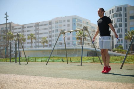 Junger, athletischer Mann beim Trainieren mit einem Springseil im städtischen Umfeld. Aktive beim Cardio-Workout, Abnehmen, Kalorienverbrennen beim Seilspringen auf dem Spielplatz im Freien