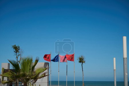 Contexte avec des drapeaux de différents pays sur la promenade. Drapeaux du Maroc, de l'Espagne, de l'Union européenne, des États-Unis et de la Grande-Bretagne sur fond bleu et océan Atlantique