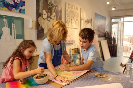 Foto de Mujer pintora inspirada enseñando a los niños a pintar sobre lienzo, compartiendo consejos y habilidades con estudiantes lindos durante la clase de arte en el taller de arte visual creativo. Desarrollar la creatividad, la imaginación. Educación - Imagen libre de derechos