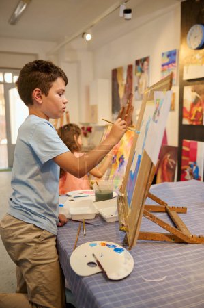 Foto de Adorables niños talentosos se concentran en la pintura acrílica a color sobre lienzo en el aula de arte. Aprendizaje creativo con talentos y habilidades en la educación en el estudio de la escuela primaria. Personas y arte visual - Imagen libre de derechos
