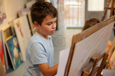 Foto de Retrato de primer plano de un talentoso pintor inspirado en un lienzo con pincel y pinturas acrílicas de colores en una clase de pintura - Imagen libre de derechos