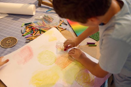 Foto de Vista aérea de un adolescente dibujando en papel con lápices de colores pastel, creando un fondo para más durante la clase de arte - Imagen libre de derechos