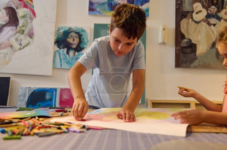 Foto de Enfocado serio adolescente colegial tomando lápiz de la pila de lápices de colores, dibujo de la imagen en la escuela de arte creativo - Imagen libre de derechos