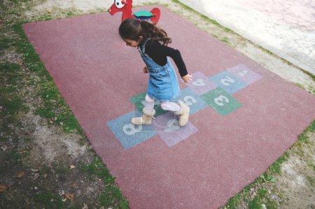 Photo for Overhead view of a little child girl jumping on squares, playing hopscotch on the school playground. Street children's games in classics. Popular street children's games in classics. Happy childhood - Royalty Free Image