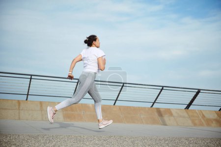 Foto de Vista desde atrás a una deportista, atleta corredor haciendo ejercicio cardiovascular, corriendo al aire libre en el puente de la ciudad. Fitness. Deporte. Concepto de estilo de vida saludable activo - Imagen libre de derechos