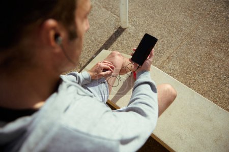 Overhead-Ansicht des jungen Mannes mit Mobiltelefon mit leeren schwarzen Attrappe Bildschirm, kopieren Werbefläche mobile App. Männlicher Athlet überprüft Fitness-Anwendung, Herzfrequenz während der Trainingspause