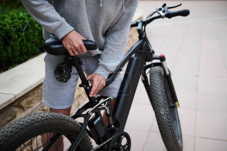 Ausgeschnittene Ansicht. Fahrradfahrer stellt vor der Fahrt einen Sitz auf einem batteriebetriebenen Fahrrad ein. E-Bike-Verleih als umweltfreundlicher Stadtverkehr. Menschen. Ein aktiver gesunder Lebensstil. Stadtleben. Nachhaltigkeit