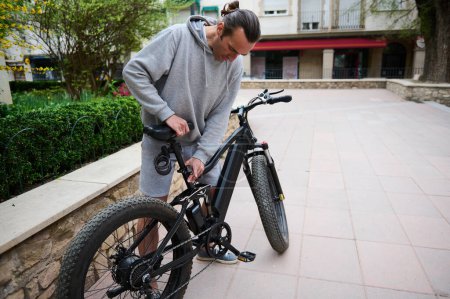 Blanc jeune homme cycliste réglage d'un siège sur vélo électrique, vélo avant de monter. Louer un vélo électrique comme moyen de transport urbain écologique. Les gens. Mode de vie sain et actif. La vie urbaine. Durabilité