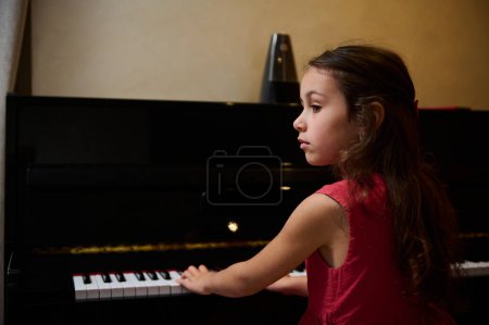 Pequeña pianista que toca el piano, canta, crea música, interpreta y compone melodía en pianoforte. La colegiala está practicando con el instrumento de acordes. Educación y entretenimiento para niños