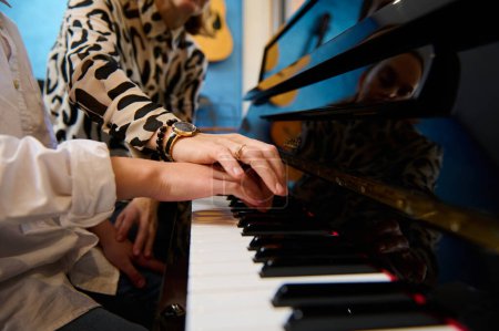 Primer plano pianista mujer músico enseñando a un adolescente estudiante la posición correcta de los dedos, sentado al piano mientras se realiza la composición musical en grand pianoforte, durante la lección de música.
