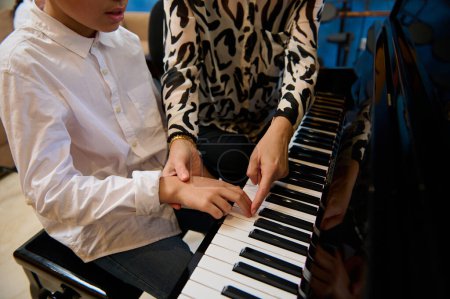 Primer plano de una pianista, profesora de música explicando las manos correctas y la posición de los dedos en las teclas de piano, enseñando lecciones de piano en casa. Crear concepto de música y canciones. Ocio y hobby en interiores.