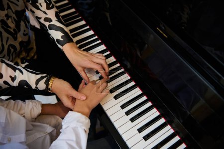 Top view hands of a musician pianist teacher maestro teaching a child boy the true position of fingers on piano keys while performing musical composition on grand pianoforte, during music piano lesson