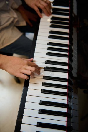 View from above of the hands of a pianist musician kid playing piano, putting fingers on white and black piano keys. Boy learning chord musical instrument during a music lesson