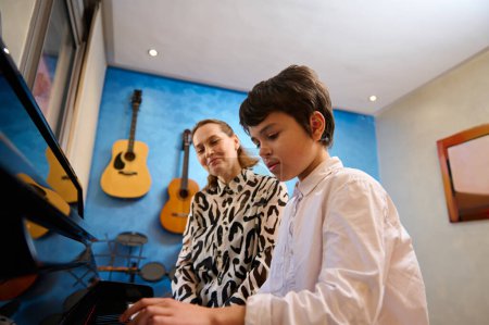 Talentierter Jugendmusiker bei einer Klavierstunde mit seinem Lehrer. Pianistin erklärt die richtige Position der Hände auf den Klaviertasten. Musikalische Ausbildung und Talententwicklung im Gange