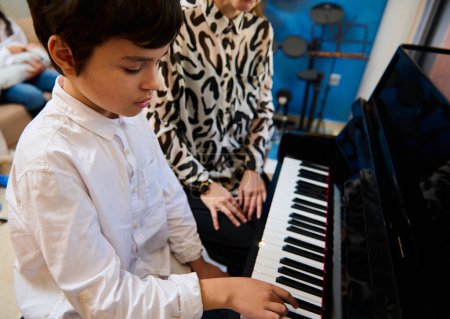 View from above of confident talented teenage musician plays piano forte, creates music and song composes a melody during music lesson. Teenager boy confidently playing grand piano during music lesson