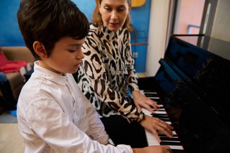 Teen boy having music lesson at home, sitting near his pianist teacher, playing piano forte. Adorable talented adolescent boy learning piano. Musical education nd artistic development of young people