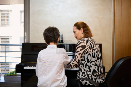 Vue arrière d'un professeur de musique expliquant une leçon de piano à son élève pendant une leçon de musique individuelle à la maison. Éducation musicale et développement artistique pour les jeunes et les enfants. Loisirs et loisirs