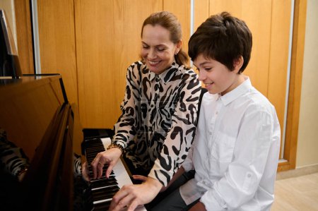 Authentique portrait d'une pianiste musicienne tenant la main d'un adolescent, montrant la vraie position du doigt sur les touches du piano, expliquant la leçon de piano pendant les cours individuels de musique à l'intérieur