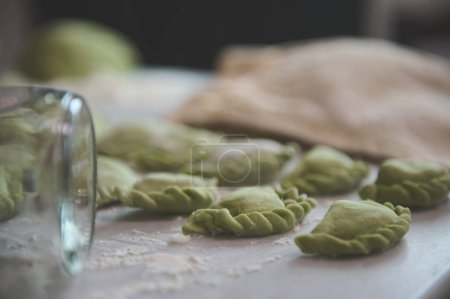 Gros plan boulettes maison de couleur verte sur une table de cuisine farinée et vue partielle d'une bouteille en verre comme rouleau à pâtisserie au premier plan. Préparation de la cuisine traditionnelle en Ukraine varennyky