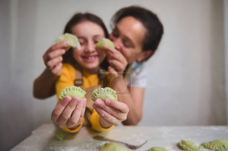 Mother and daughter playing together in the kitchen, having fun while enjoying cooking homemade dumplings for family dinner. Selective focus