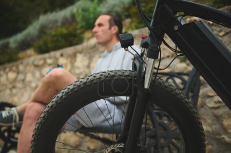 Selective focus on tubeless tire of an electric motor bike, mountain bike over blurred background of a male cyclist in the city