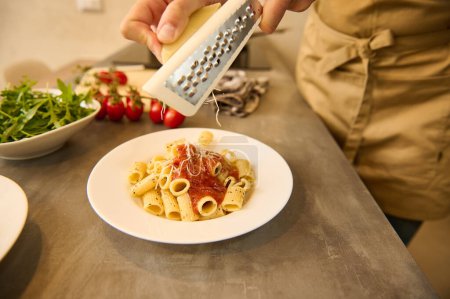 Male chef seasoning Italian pasta with grated cheese. Culinary. Epicure. Cooking. Food background