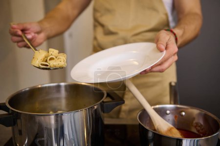 Close-up male chef standing at stove and putting freshly cooked pasta penne on a white plate. Food concept