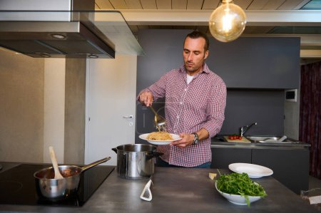Authentic portrait of a handsome guy at home kitchen, plating up freshly cooked spaghetti, preparing healthy dinner for family, according to traditional Italian. People. Food and drink consumerism