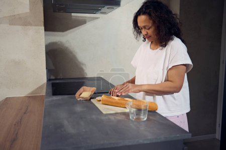 Seitenporträt einer Frau, die ein Küchenmesser benutzt, einen Laib französisches Baguette-Vollkornbrot auf dem Schneidebrett schneidet, leckere Sandwiches mit Käse für das Frühstück in der heimischen Küche zubereitet.